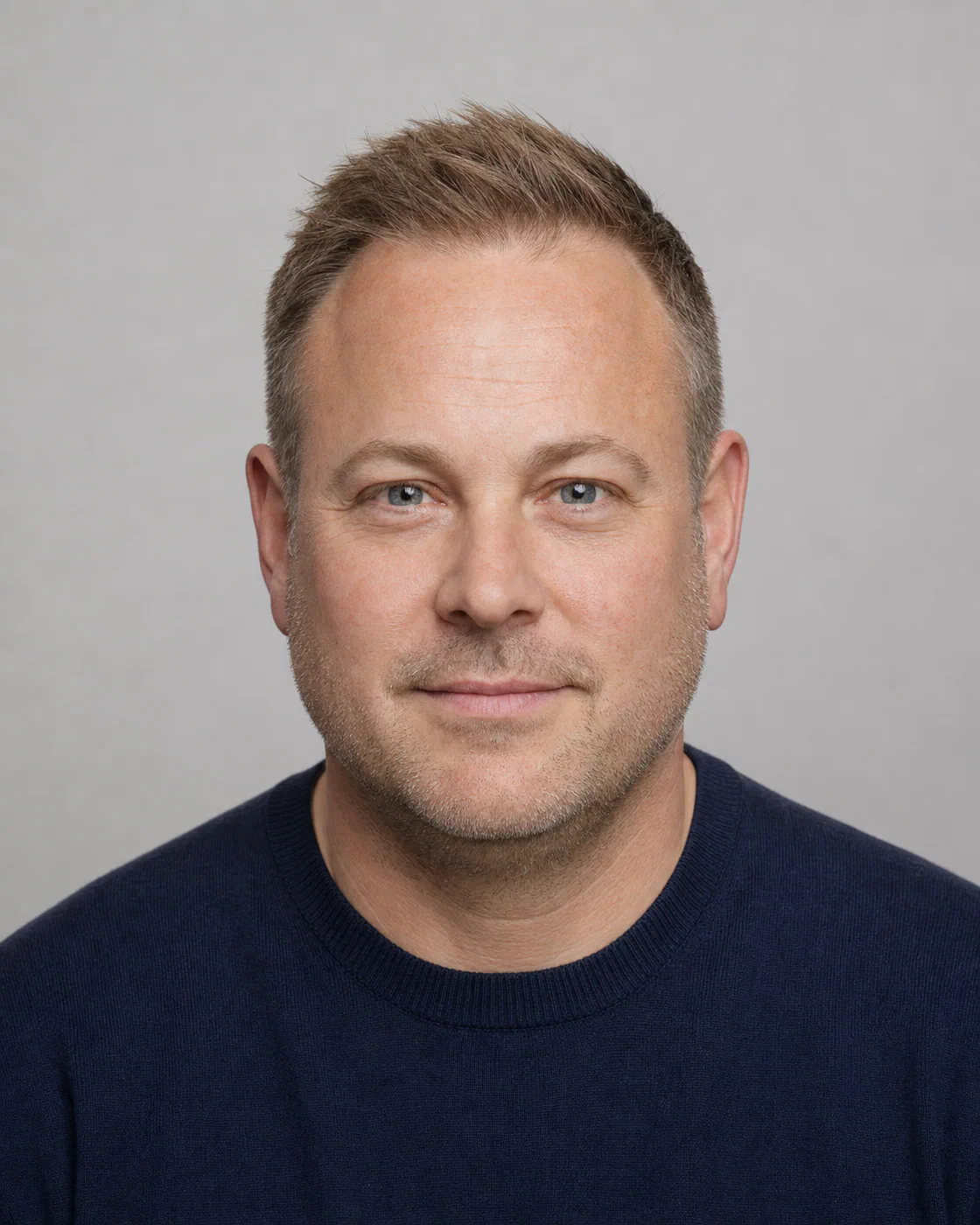 A mature man with a round face and fine hair wearing a short Ivy League brush-up