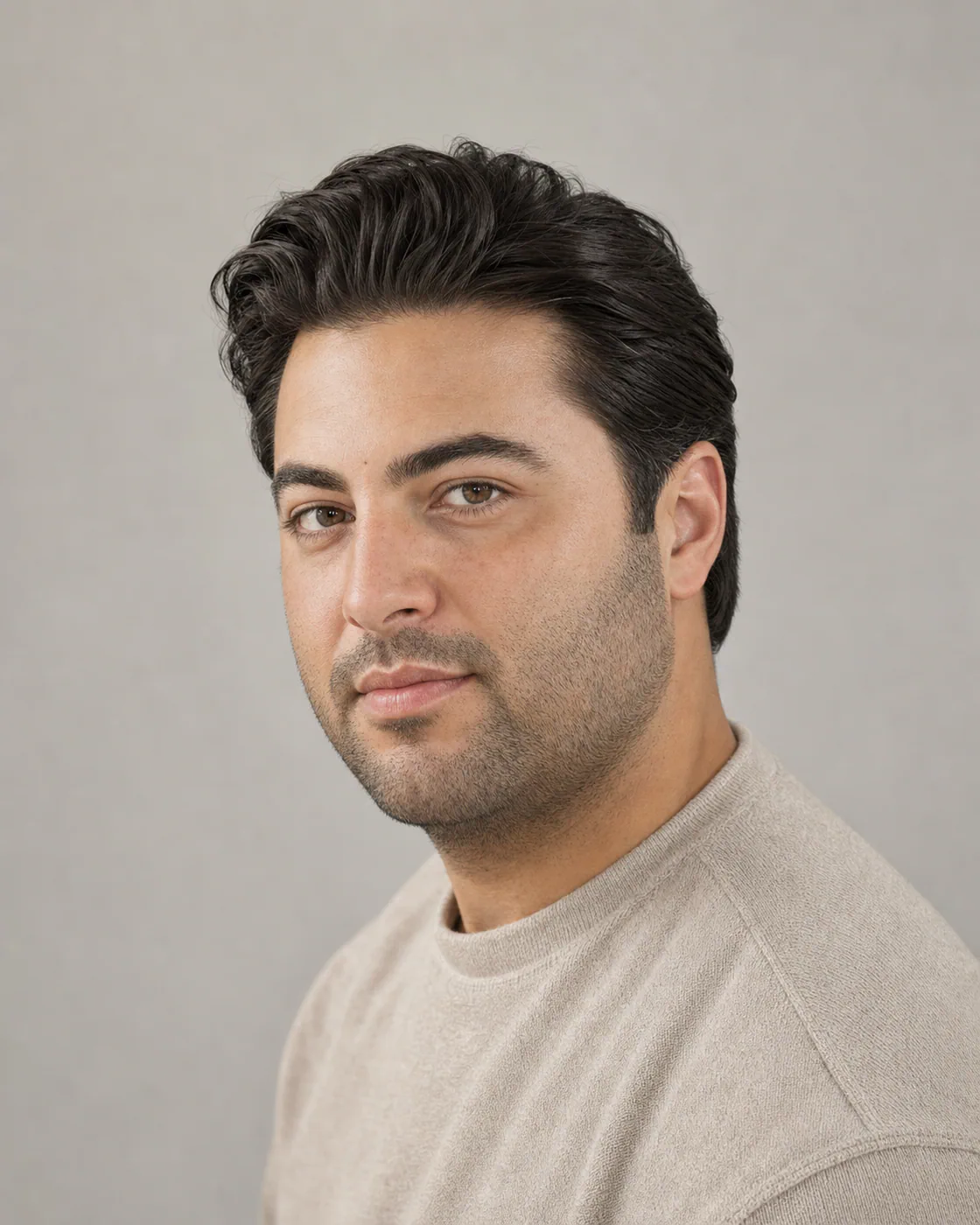 A man with a round face wearing a loose matte slick back with lifted roots