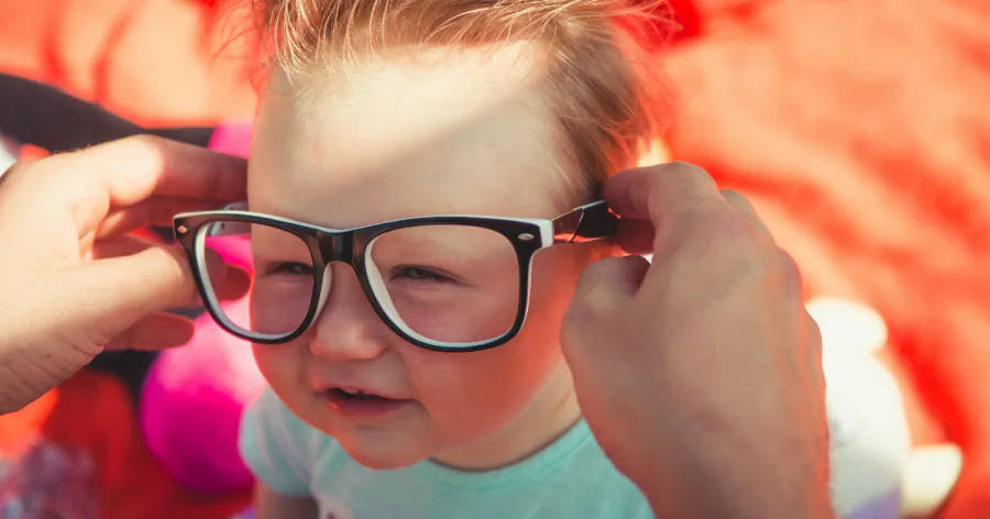 A baby trying on oversized black glasses