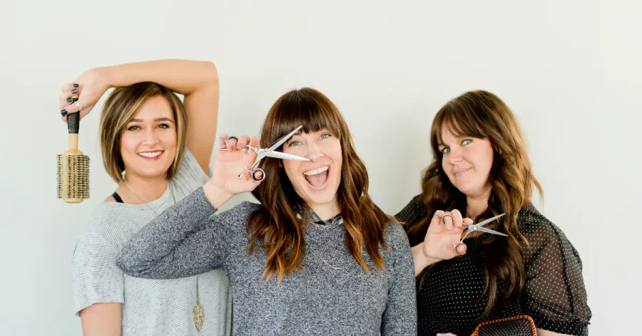 Three hairstylists holding brushes and scissors